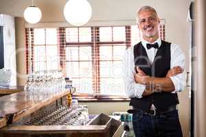 Portrait of smiling bartender standing with arms crossed