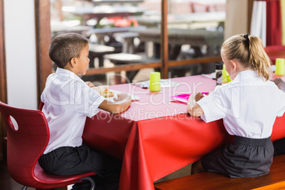 Boy and girl in school uniforms having lunch in school cafeteria