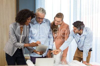 Businesswoman and coworker discussing blueprint on the desk usin