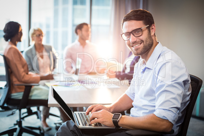 Man using laptop while coworker interacting in the background