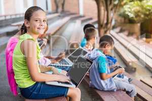 Kids sitting on bench and using laptop