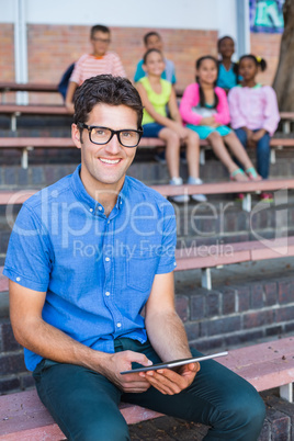 Portrait of teacher sitting on bench and using digital tablet