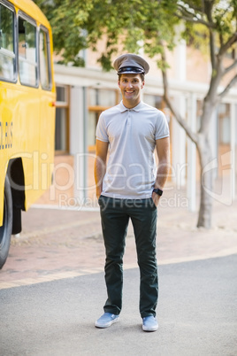 Smiling bus driver standing with hands in pocket in front of bus