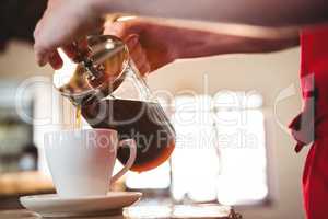 Mid section of waiter pouring a cup of coffee