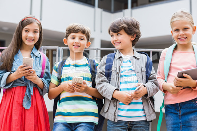 Kids holding mobile phone and digital tablet standing on school