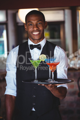 Portrait of bartender holding serving tray with cocktail glasses