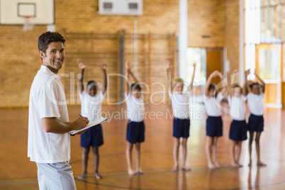 Sports teacher writing notes on clipboard while students exercis