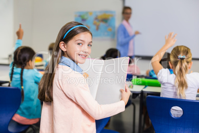 Portrait of schoolgirl standing with book in classroom