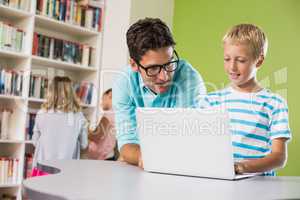 Teacher and schoolboy using laptop in library