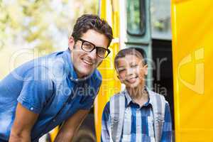 Smiling teacher and schoolboy standing in front of school bus