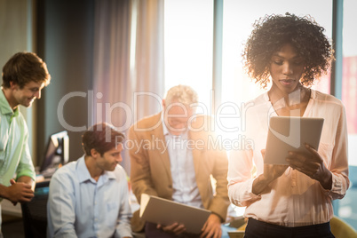 Businesswoman working on digital tablet with coworker in backgro