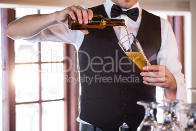 Mid section of bartender pouring a beer in a glass