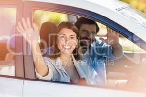 Happy couple waving hands while in car