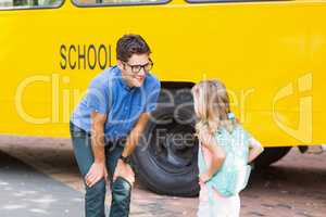 Teacher and schoolgirl interacting in front of school bus