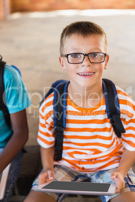 Smiling schoolboy using digital tablet at school