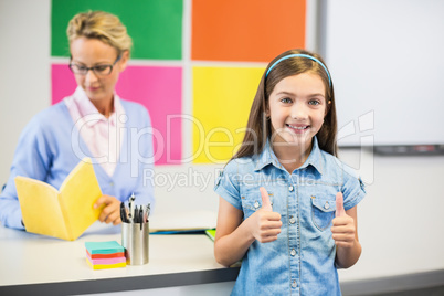 Schoolgirl showing thumbs up in classroom