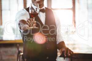 Mid section of bartender offering a glass of wine at bar counter