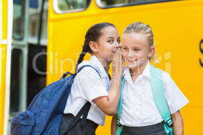 Smiling schoolgirl whispering in her friend's ear