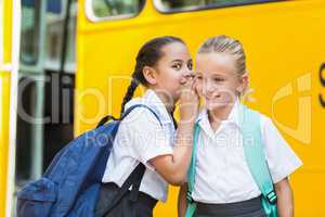 Smiling schoolgirl whispering in her friend's ear
