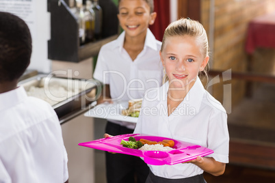 Smiling schoolgirl holding food tray in school cafeteria