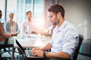 Man using laptop while coworker interacting in the background