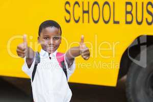 Smiling schoolboy showing thumbs up in front of school bus