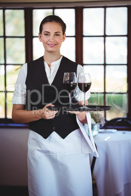 Smiling waitress holding a tray with glasses of red wine