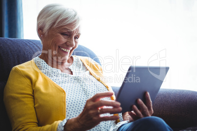 Smiling senior woman looking and laughing at her digital tablet