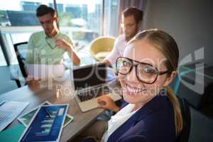 Businesswoman smiling at camera while her colleagues reading doc