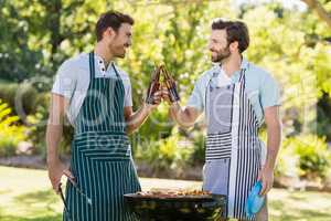 Men toasting beer bottle while preparing barbecue grill