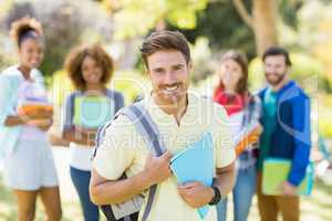 Portrait of college boy holding notes with friends in background