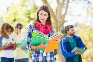 College girl reading notes with friends in background