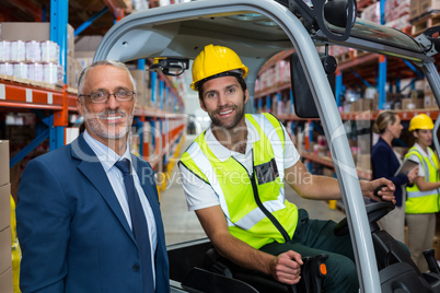 Worker driving forklift looking at camera with businessman