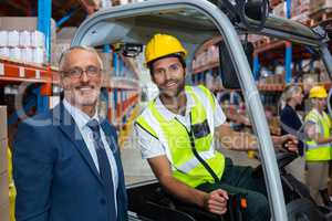 Worker driving forklift looking at camera with businessman