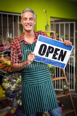 Male florist holding open signboard at flower shop