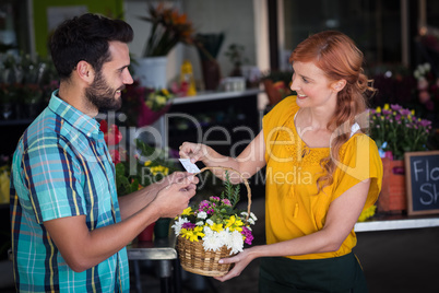 Female florist giving visiting card and flower basket to custome