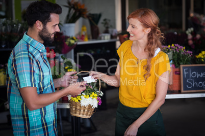 Female florist giving visiting card and flower basket to custome