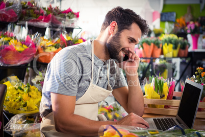 Male florist talking on mobile phone while using laptop