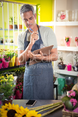 Thoughtful male florist looking reading clipboard