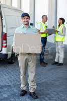 Delivery man is holding a cardboard box and smiling to the camer