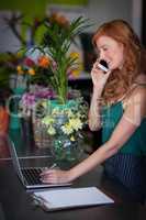 Female florist talking on mobile phone while using laptop