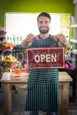 Male florist holding open signboard at his flower shop