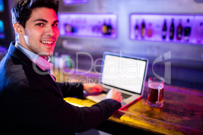 Smiling man using laptop with glass of beer on table at bar coun