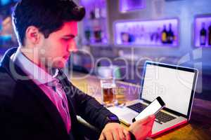 Man using mobile phone with glass of beer and laptop on table at