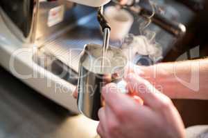 Waiter steaming milk at the coffee machine