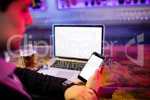 Man using mobile phone with glass of beer and laptop on table at