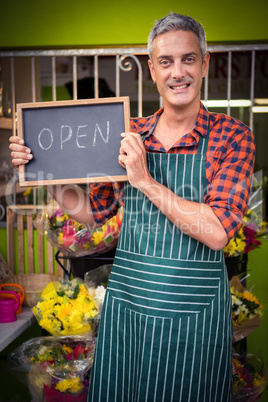 Male florist holding open sign on slate at his flower shop