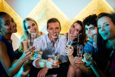 Group of smiling friends sitting on sofa and having a glasses of