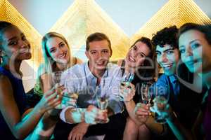 Group of smiling friends sitting on sofa and having a glasses of