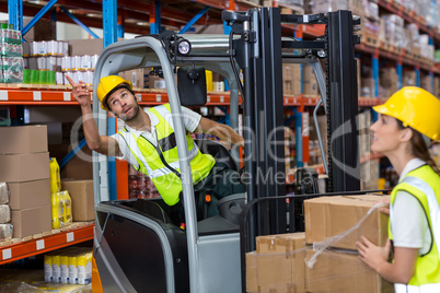 Focus of worker sitting on a pallet truck is pointing shelves